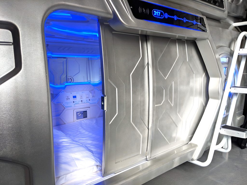Interior of a private capsule hotel pod at MET A Space Pod with a made bed and ambient lighting
