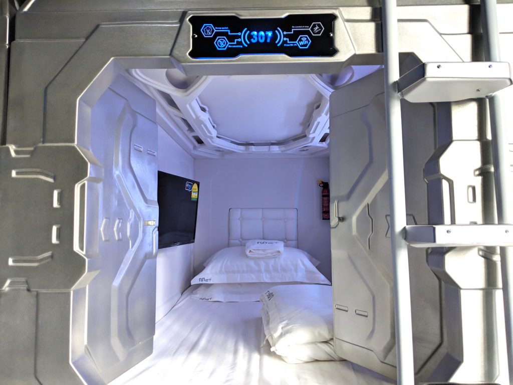 Interior view of a single capsule pod at MET A Space Pod, showing the bed, personal screen, and entrance