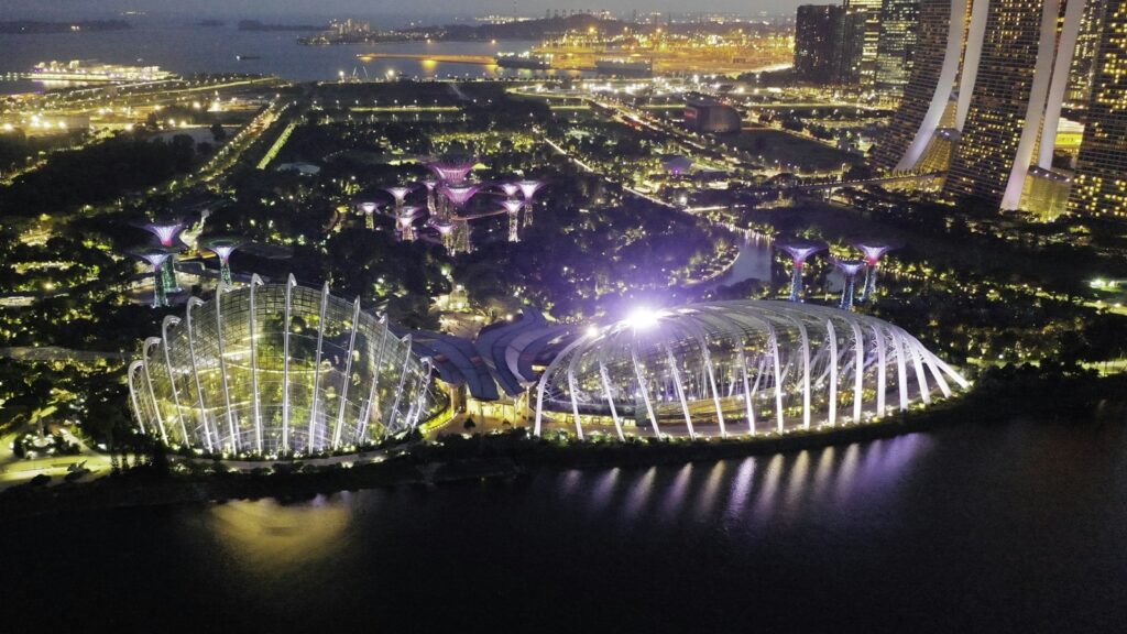 Aerial night view of Gardens by the Bay’s Supertree Grove and conservatories with Marina Bay Sands in the background, Singapore