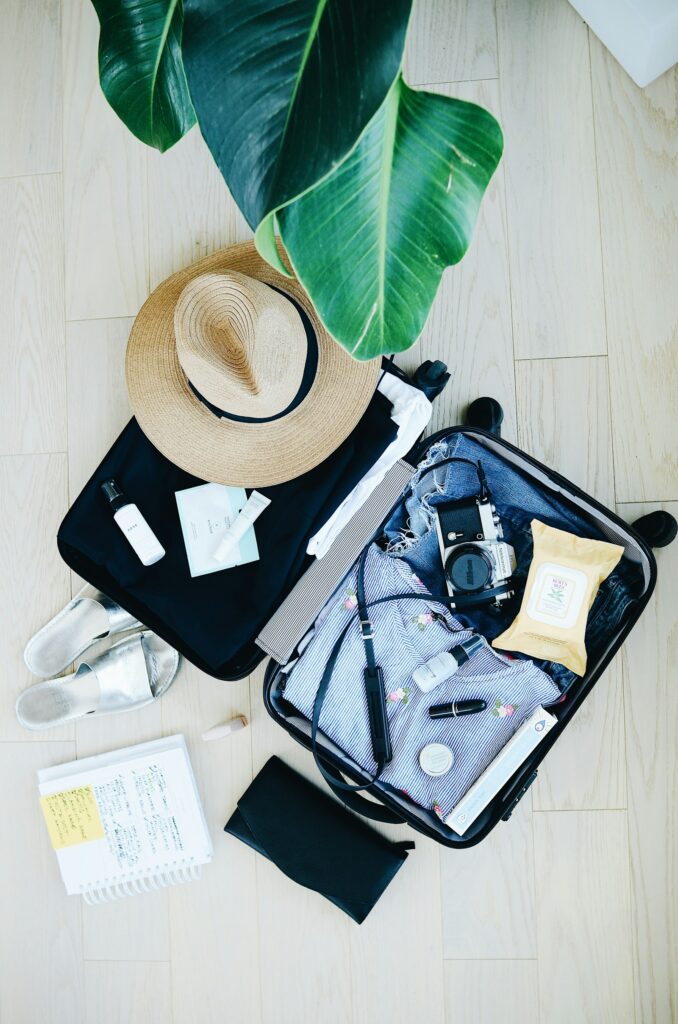 Flatlay of an open suitcase packed with travel essentials, a sun hat, and a camera